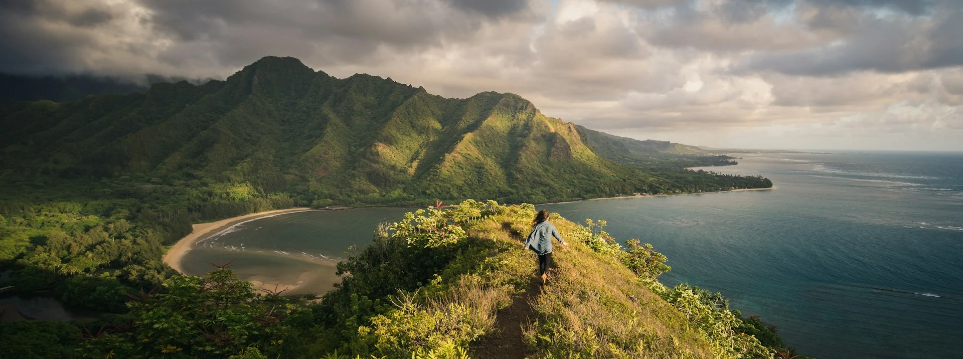 Hiker on tropical ridge trail overlooking coastal bay — warm exposed terrain the Hoka Speedgoat 6 is built for